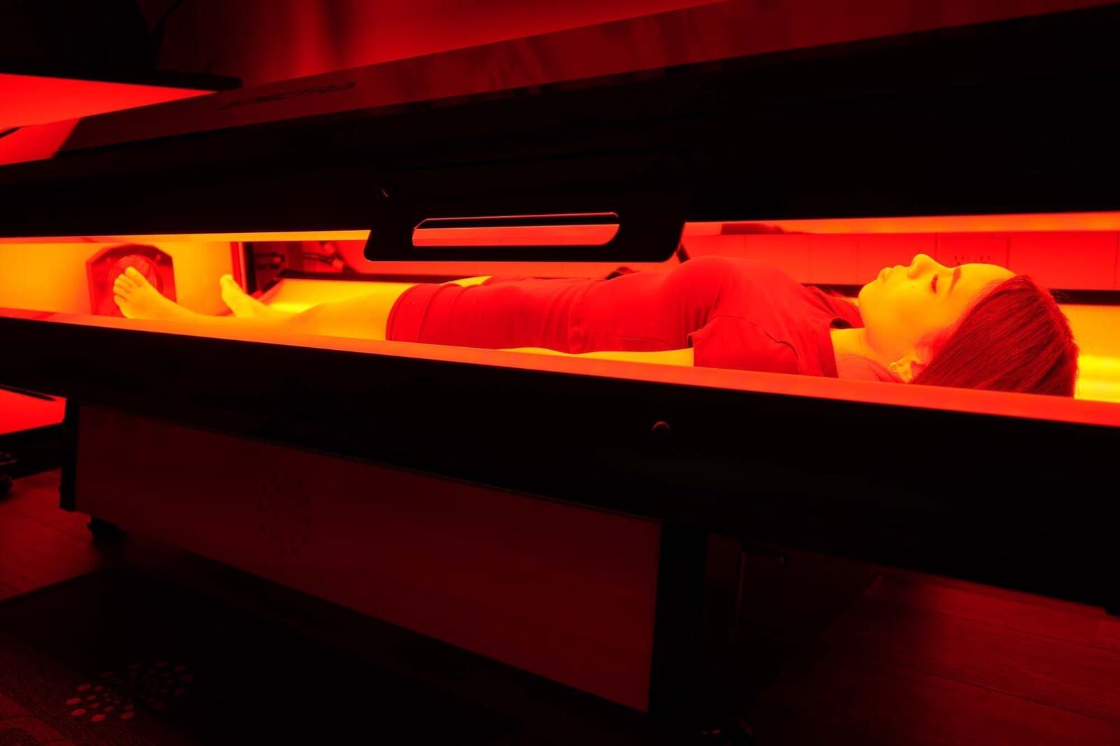 A guest lying in the Spectra S10 Pro red light bed with the lid lowered and the red light panels glowing above and below her