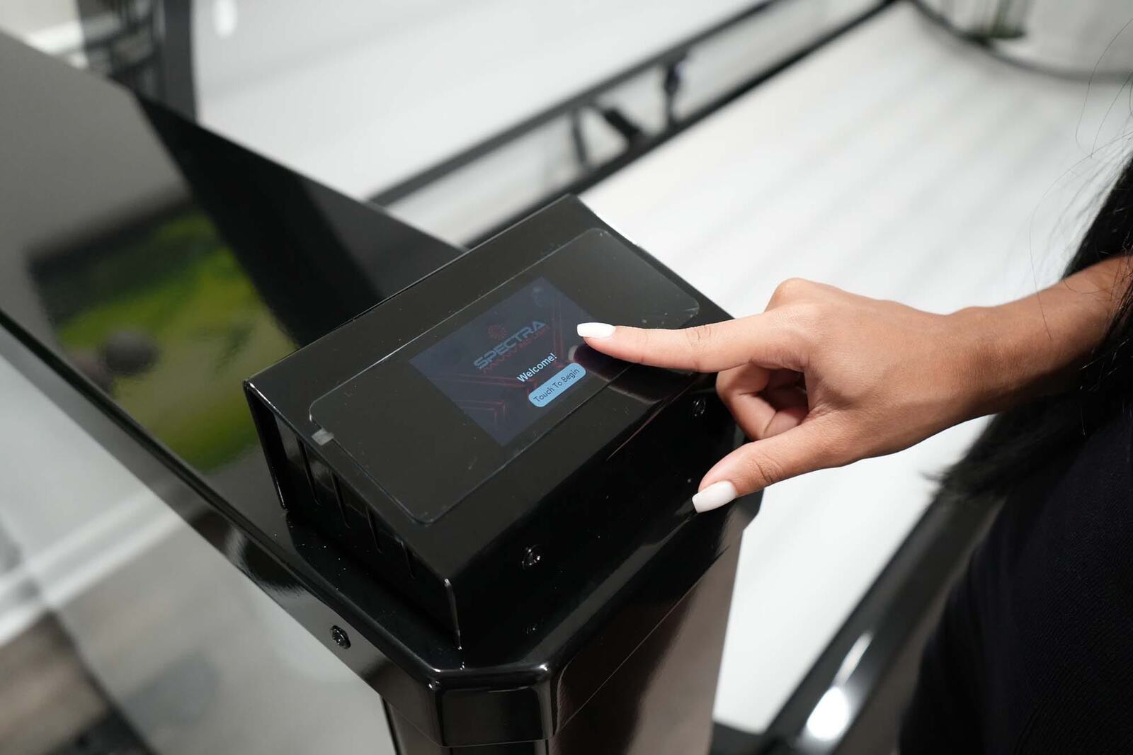 A finger tapping the Spectra touch screen on the side of the red light bed, which shows Welcome and Touch To Begin
